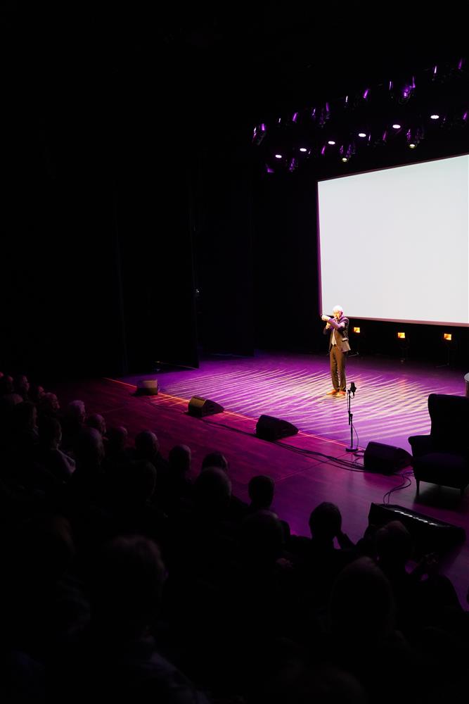 En mann på scenen som spiller horn, masse publikum i salen. - Klikk for stort bilde