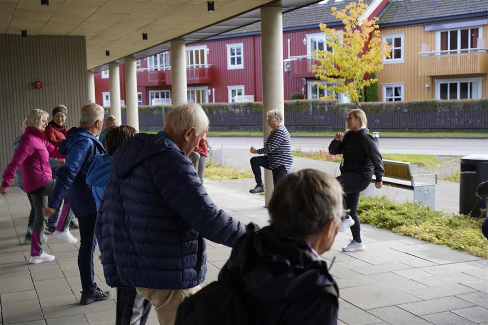 En gruppe eldre men instruktør som har trim rett utenfor helsehuset med aktivitetsgruppa «Trim og trivsel». - Klikk for stort bilde
