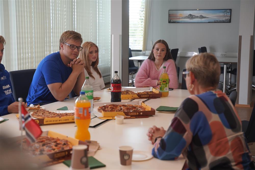 Ungdomsutøvere, ordføreren samt frivillige sitter rundt bord i formannskapssalen, de spiser pizza og drikker brus. - Klikk for stort bilde