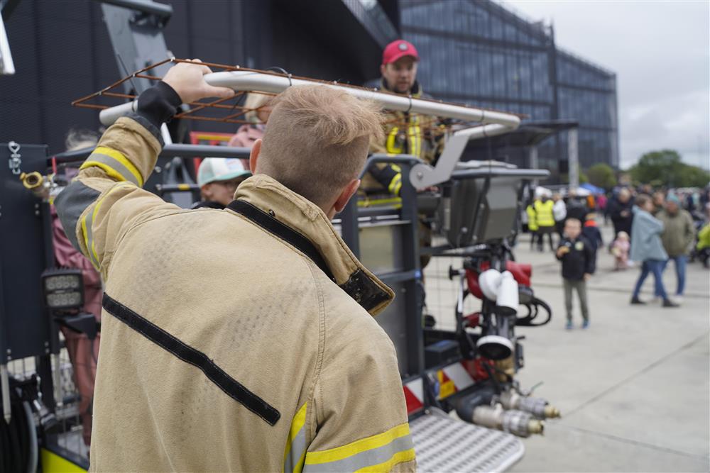 To brannkonstabler som hjelper barn og foreldre opp i liften til brann- og redning. En passer på at alle kommer seg inn, en kjører liften. - Klikk for stort bilde