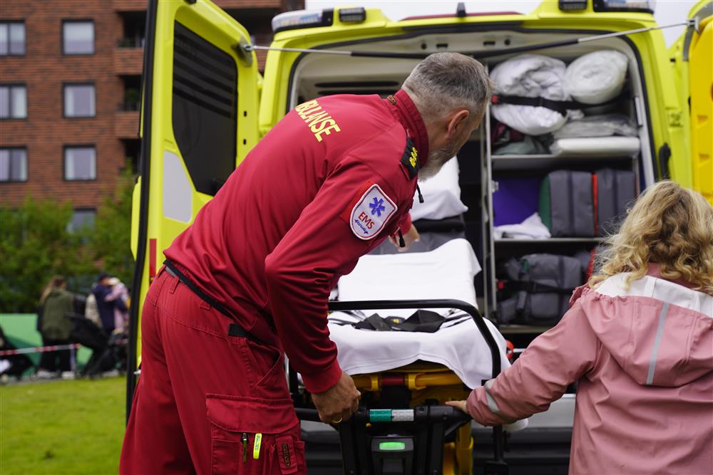 En mannlig ambulansearbeider som viser en jente hvordan man dytter inn en båre i en ambulanse. - Klikk for stort bilde