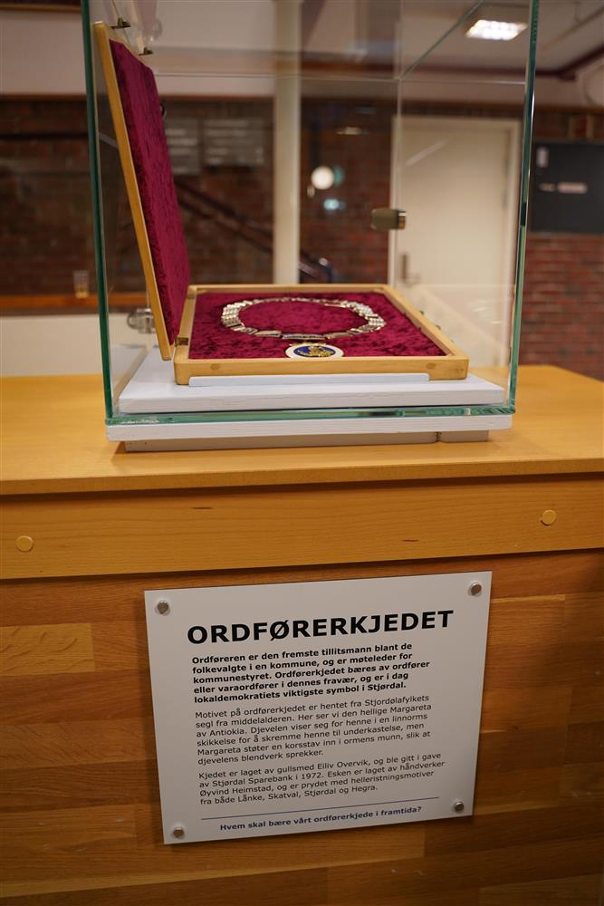 Et glassmonter med ordførerkjedet i og en tekstplakat under - Klikk for stort bilde
