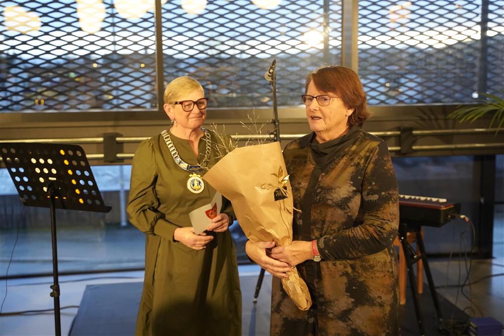 To damer på en scene, fra venstre ordføreren som har på seg ordførerkjedet og smiler. Til høyre står Ingrid Sandvik som er datteren til Svanhild og tok tatt imot blomster - Klikk for stort bilde
