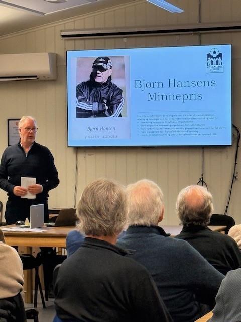 En man som prater til en forsamling, han viser en power point på et lerret. Det vises en side med informasjon om Bjørn Hansens Minnepris. - Klikk for stort bilde