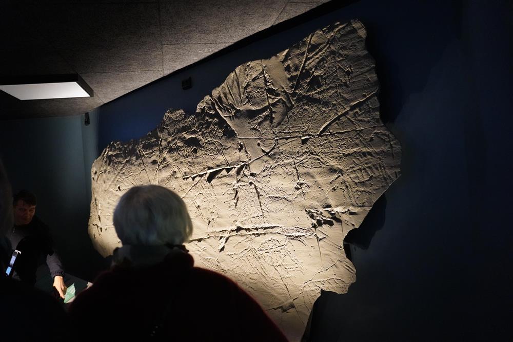 En steinvegg med bergkunst inne på senteret, to personer står å ser på de. - Klikk for stort bilde