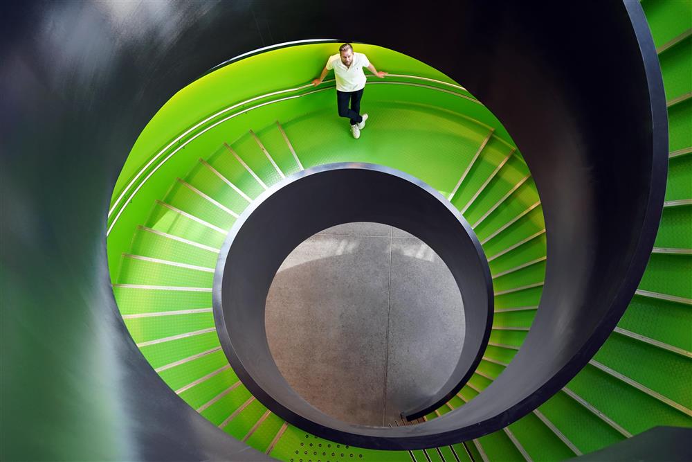 En man som står i en grønn trapp, han står et stykke unna og ser opp, trappen går i en spiral nedover - Klikk for stort bilde