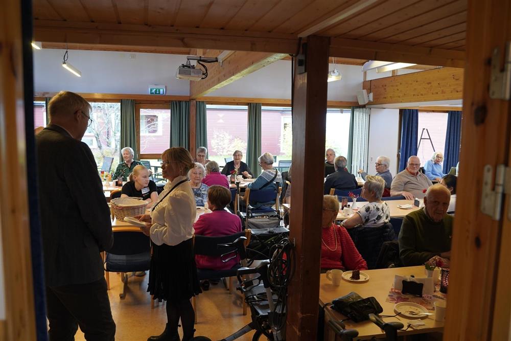 Eldre som sitter rundt flere bord og spiser kake og drikker kaffe på Stjørdal Aktivitetsenter. - Klikk for stort bilde