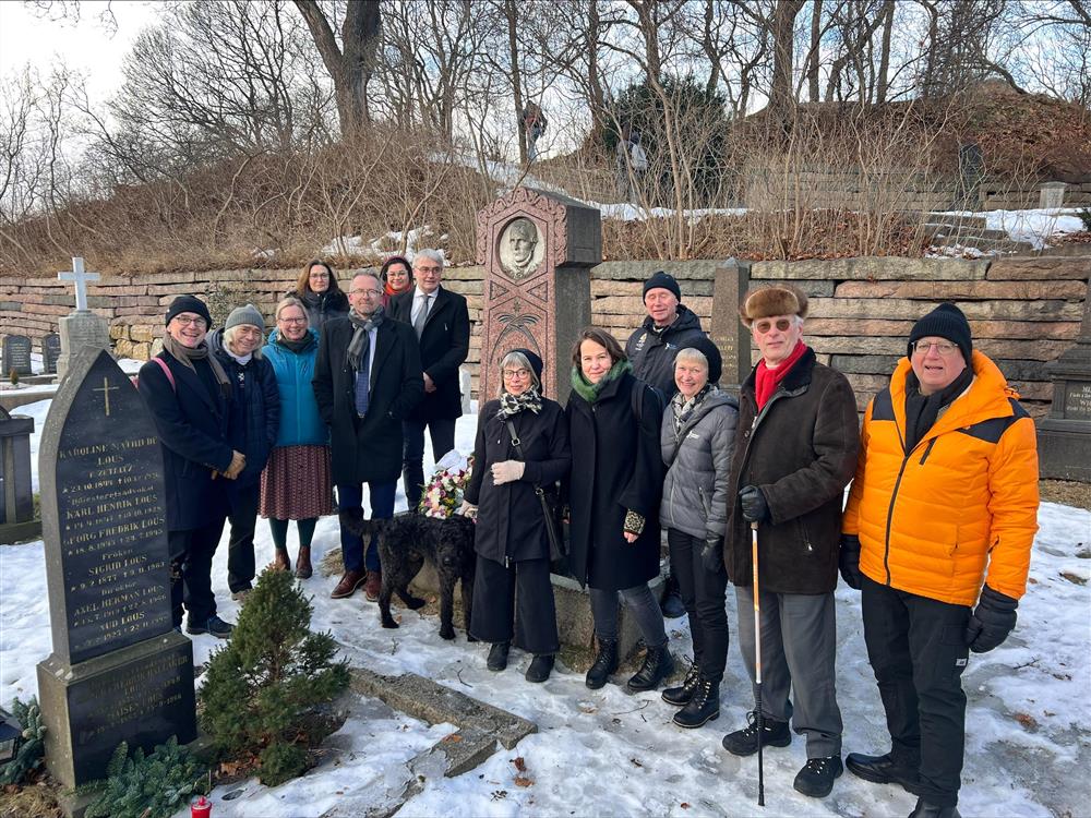 14 personer utendørs foran graven til Ole vig, det er snø men ellers fint vær. - Klikk for stort bilde