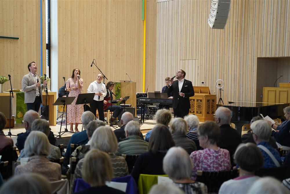 To menn og en dame som synger fra scenen i Stjørdal kirke. - Klikk for stort bilde