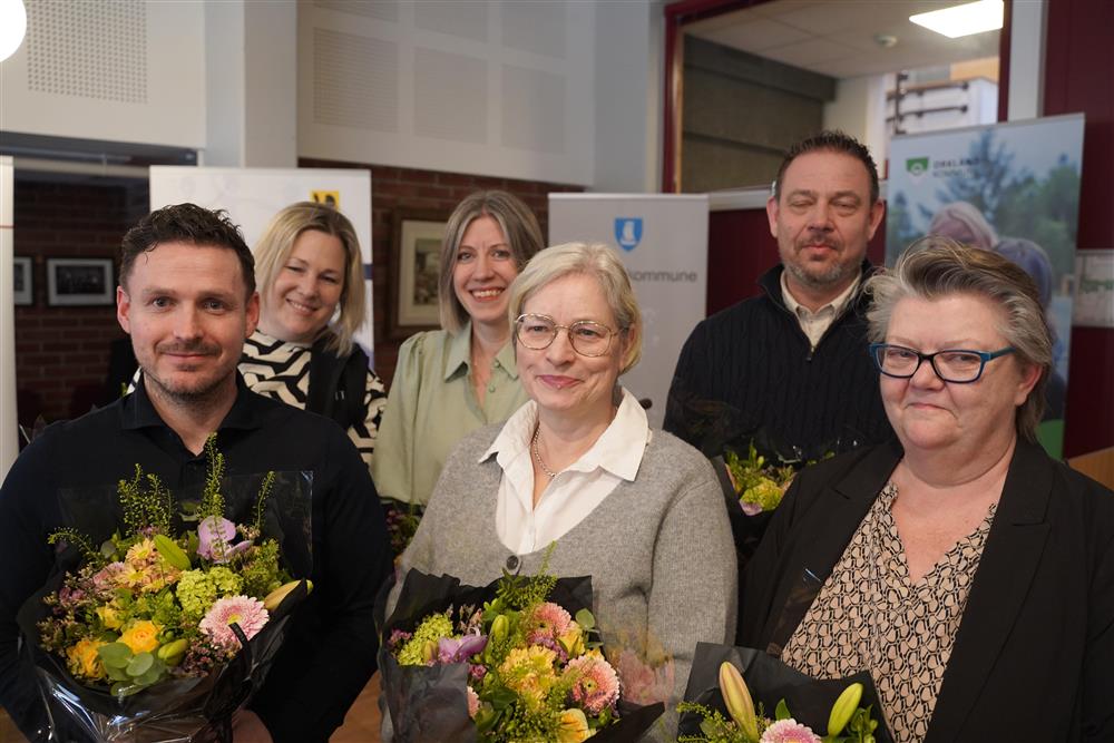 De seks personene som har sittet i prosjektgruppa som smiler til kamera, de har fått blomster. - Klikk for stort bilde
