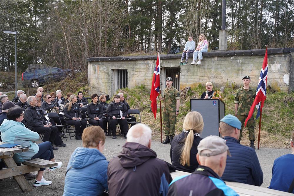 Ordfører Eli Arnstad står bak podiumet og holder sin tale. På hver side står en flaggbærer, til venstre sitter korpeset, i front sitter publikum. - Klikk for stort bilde