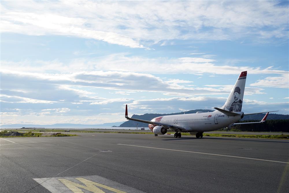 Et Norwegian fly på vei bortover rullebannen, det er sett bakfra. Det er strålende sol, blå himmel og noen små skyer - Klikk for stort bilde