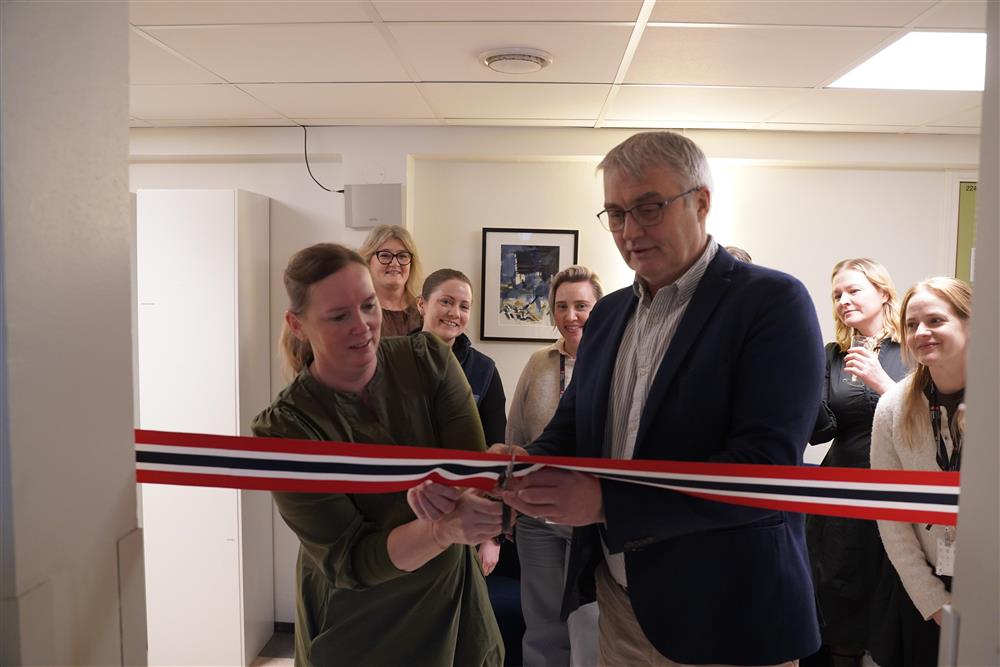 Kommunedirektør og prosjektleder som klipper en snor med fargene til det norske flagget, i bakgrunnen står flere ansatte å ser på. - Klikk for stort bilde