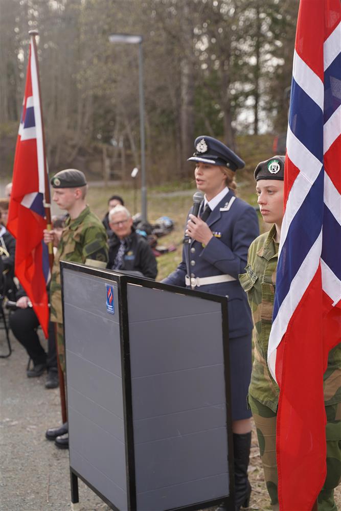 Stabsjef og oberstløytnant Marianne Eidem holder sin tale. Hun står bak et podium, på hver side av henne står en flagbærer fra HV-ungdom. I bakgrunnen sitter korpset.  - Klikk for stort bilde
