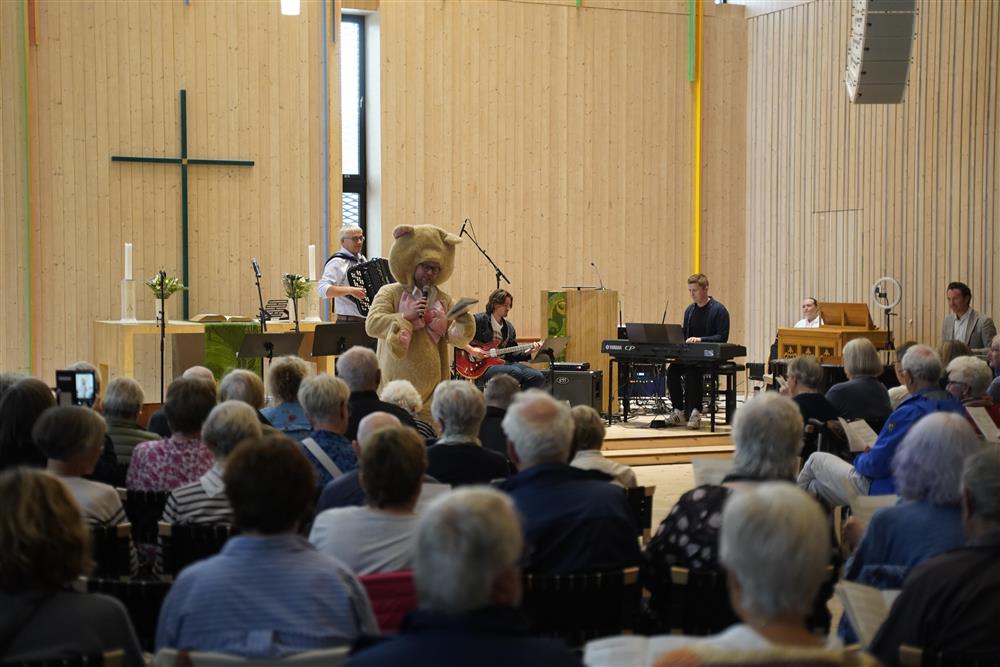 En mann i Teddybjørn drakt som synger, i bakgrunnen er bandet samt kommunedirektøren på trekkspill. - Klikk for stort bilde