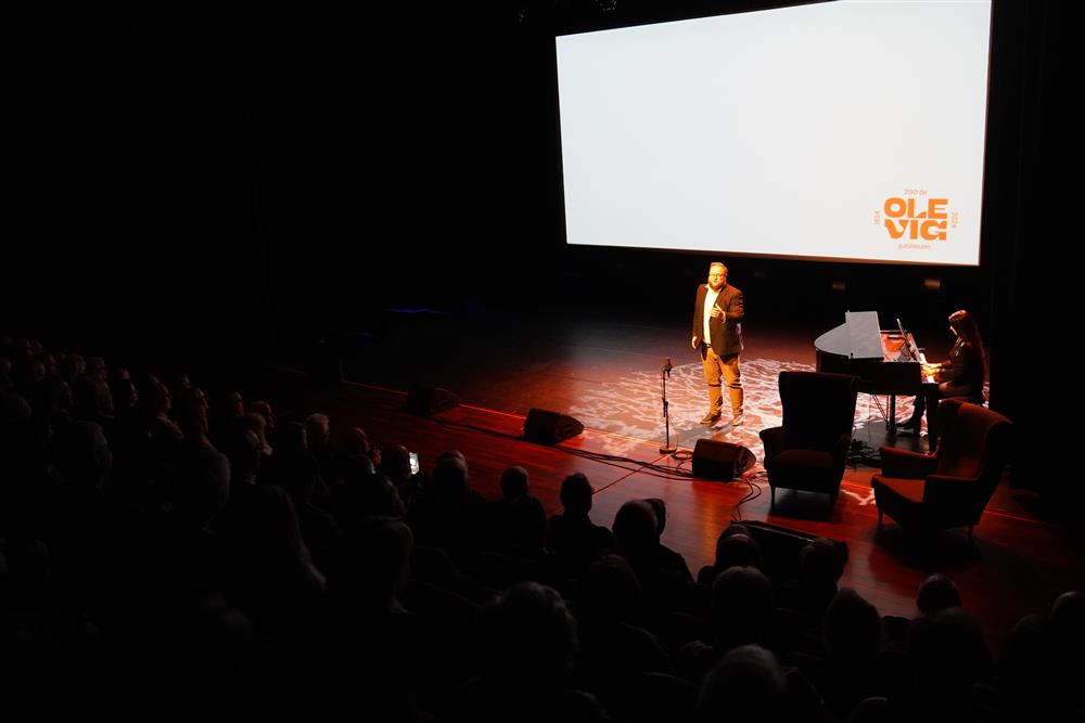 En mann på scenen som synger opera, samt en dame som spiller piano. - Klikk for stort bilde