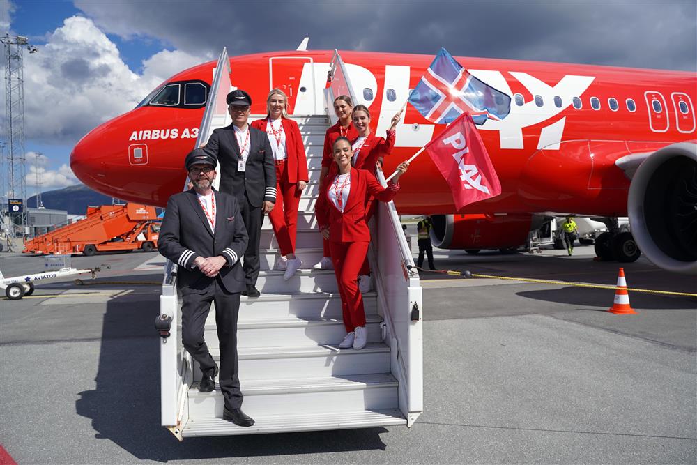 Mannskapet på flyet, to menn og fire damer. Mennene i pilot uniformer, dammene i røde flyvert uniform. De står i trappen opp til flyet, to av flyvertene har flagg. En det Islandske, en annen flagget med logoen til flyselskapet Play. - Klikk for stort bilde
