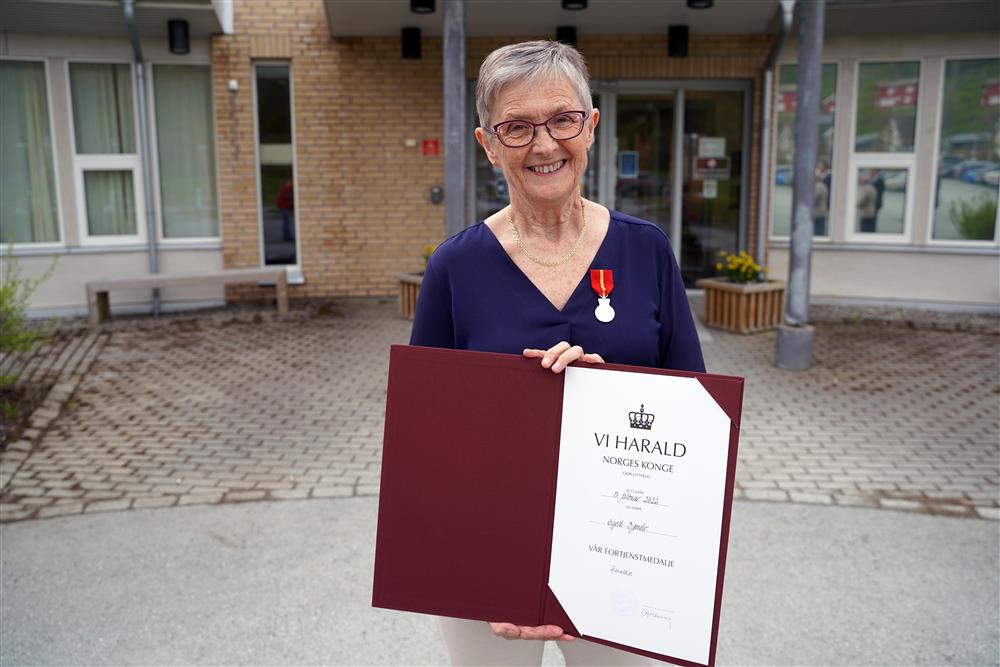 En dame som står utenfor DPS Stjørrdal og viser fram diplomet hvor det står &quot;Kongens fortjenestemedalje&quot; - Klikk for stort bilde