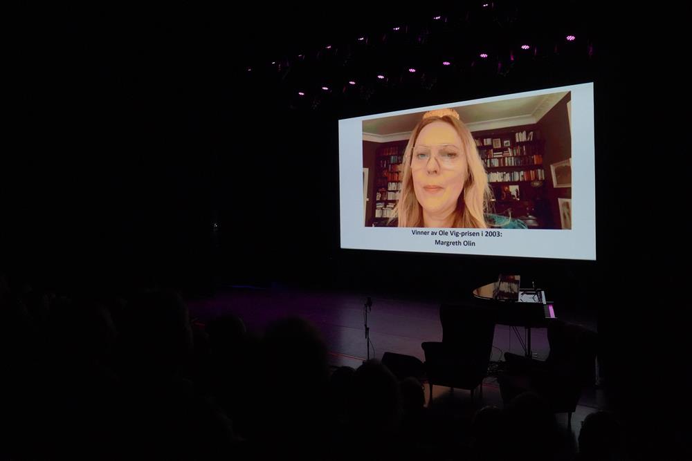 En video på storskjerm i storsalen. Margreth Olin er på skjermen. - Klikk for stort bilde