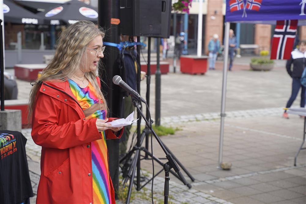 En dame i regnbuekjole som holder appel på torget. - Klikk for stort bilde