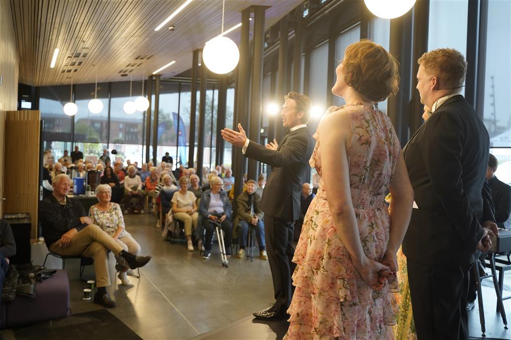 Fire operasangere på scenen i foajeen, det er fult av publikum som ser på. - Klikk for stort bilde