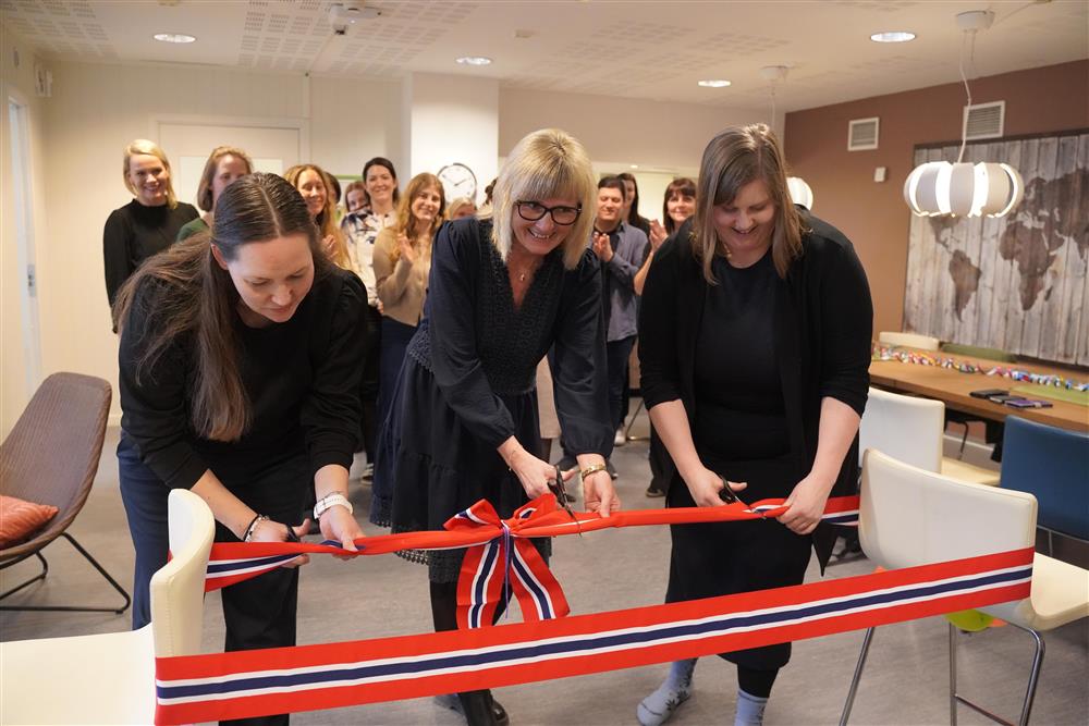 Tre damer som står sammen og klipper et bånd i rødt, hvit og blått. I bakgrunnen står det mange ansatte å følger med - Klikk for stort bilde